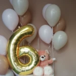 Geburtstags Dekoration zu einem 6-jährigen Geburtstag. Kombination aus einem goldenen Folien-Ballon mit der Zahl 6 und mehreren Gas befüllten Latex-Ballons in weiß und pastell-braun, sowie einem kleinen Teddybären aus Plüsch Zusammenstellung von mehreren Ballons zum 6. Geburtstag. Aus goldenen Folien-Ballon und gasgefüllte Latex-Ballons in weiß und creme-brauner Farbe