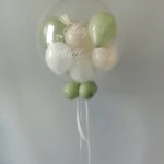 Herzlich Willkommen Ballon als Aqua Bobo Ballon mit kleinen Ballons innen in den Farben Pastell Grün, weiß und creme Aqua-Ballon mit weißem Herzlich Willkommen Aufdruck und kleinen Pastell farbigen und weißen- und cremefarbenen Ballons innen