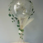 Ständer für Tisch Dekoration mit einem transparenten Aqua-Ballon der mit goldenem Konfetti gefüllt ist Aqua Ballon mit Felder und grünen Blättern dekoriert